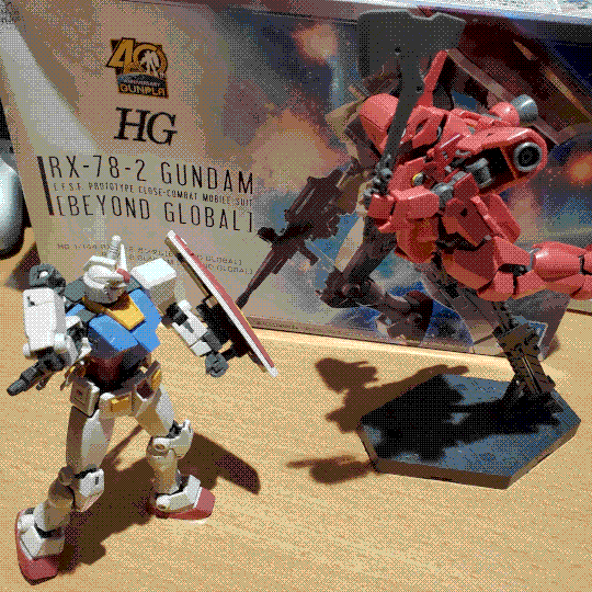 A photo of the RX-78-2 Gundam model kit posed opposed to a Graze Custom II (an angluar, red mobile suit from Gundam: Iron Blooded Orphans). The Gundam is dyanmically posed, braced with its shield in front of it and reaching behind its back to grab a beam saber. The Graze is on a raised stand, posed as if it is flying down at the Gundam and holding an axe ready to strike the Gundam.