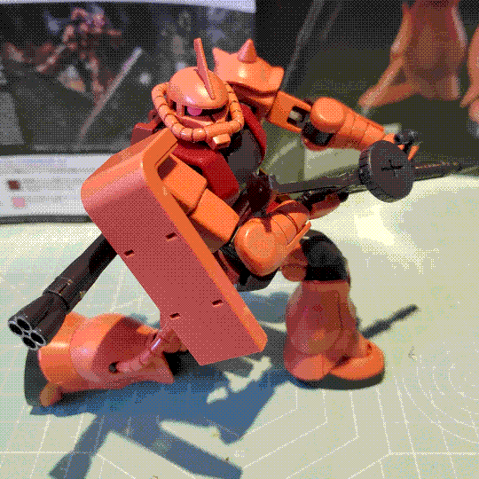 A photo of the Char's Zaku II model kit. It is posed kneeling down on one knee, with its head and eye swivelled to the side as if it has stopped mid-movement to survey its surroundings. One end of the bazooka can also be seen attached to its back.