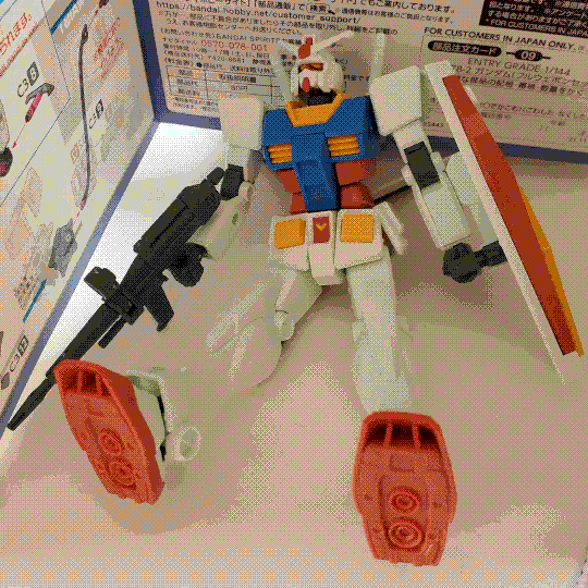 A photo of the RX-78-2 Gundam entry-grade model kit. It is posed splayed out on the ground: the bottom of the feet are visible, showing molded thruster detail, but otherwise it shows much the same parts of the kit as the photo with it standing up.