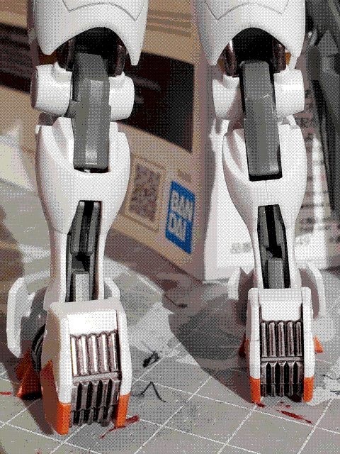 A photo showing the back of the legs of the Gundam Aerial. The legs have white armor pieces over a grey frame, and the soles of the feet are red. Parts of the frame such as pipes and vents have been detailed in metallic gunmetal paint.