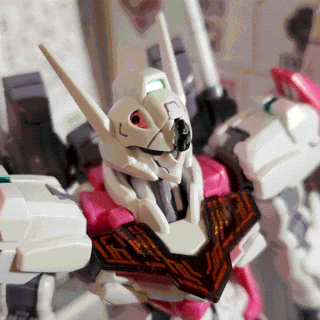 A close-up picture of the Gundam Lfrith model kit head and upper torso. The head is sharp and angular, with a pointed chin and two long, swept-back antennae. It also has a pair of recessed cavities for the vulcan cannons, highlighted in pink (only one is visible from the camera angle). The chest has smoky plastic effect piece with orange-red effect piece to appear like active Permet parts from the show.