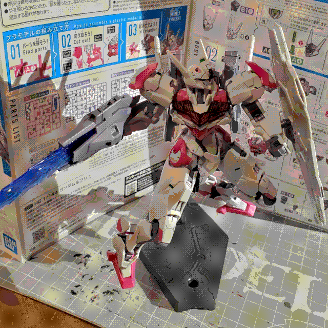 A picture of the high-grade Gundam Lfrith plastic model kit. It is a humanoid mech which is mostly white with pink accents. It is holding a shield composed of multiple parts in its left hand and a futuristic, boxy gun in its right. It is on a raised display stand and posed dynamically so that it's covering itself with the shield.