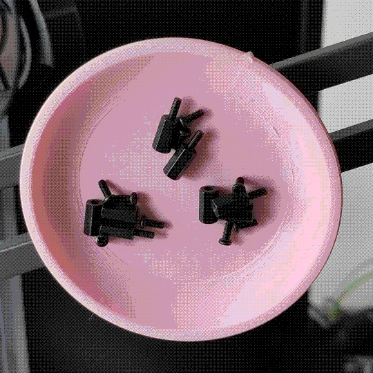 A photo of a pink dish mounted sideways to some sort of dark grey pair of bars. An asssortment of bolts and hardware is held in the dish (concentrated into three particular spots), suggesting that the dish is magnetic.