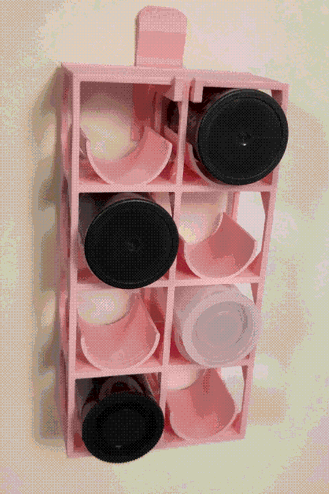 A noticeably-dithered photo of a pink film canister rack being held on a wall by the pink wall hook. The two arms of the wall hook go around a central structural member on the film rack.