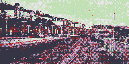 A low-resolution, heavily dithered, and purple-tinted photo of train tracks going into the distance near a town.